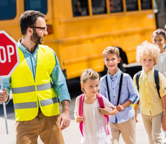 handsome traffic guard crossing road with pupils in front of school bus